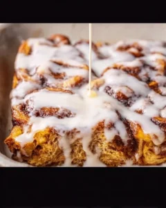 Cinnamon roll breakfast bake topped with icing and berries on a plate.