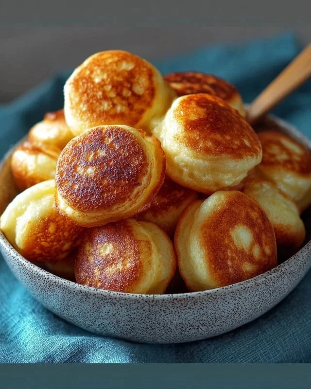 Fluffy breakfast pancake poppers served on a plate with syrup and berries.