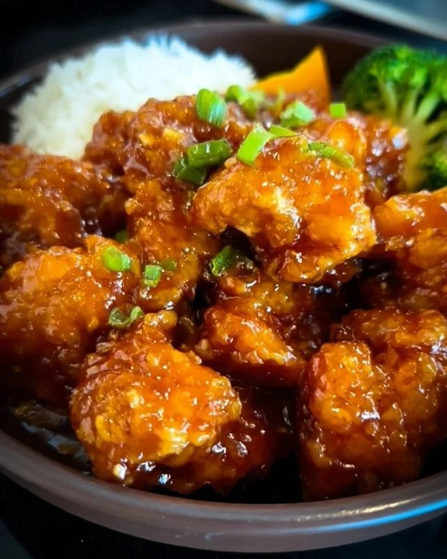 Delicious plate of orange chicken garnished with green onions and sesame seeds.