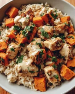 Healthy chicken and sweet potato rice bowl garnished with vegetables.