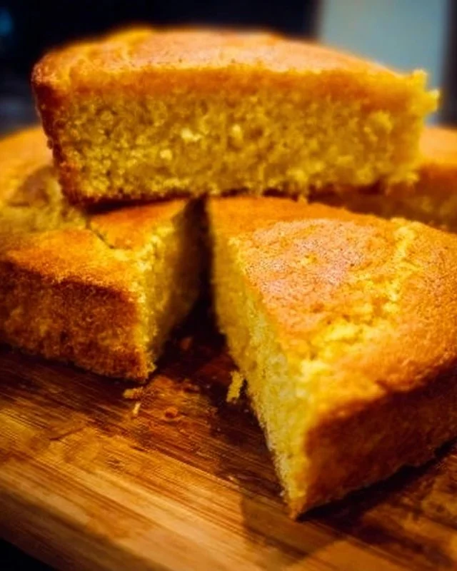 Delicious slice of Nana's famous cornbread served with butter on a wooden table.