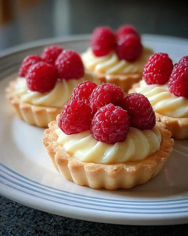Vanilla cream tarts topped with fresh raspberries on a dessert plate