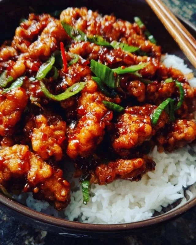 A plate of spicy dragon chicken garnished with herbs and served with rice.