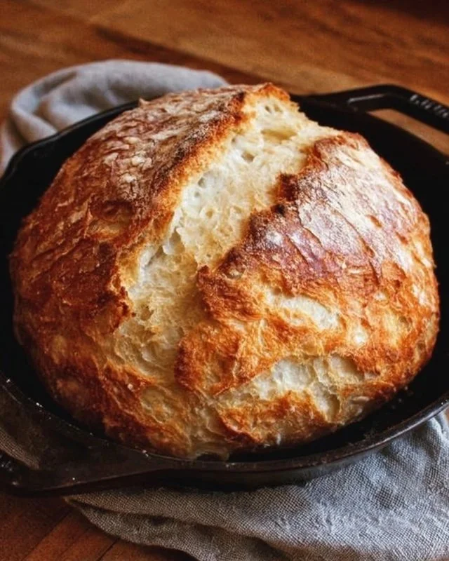 Freshly baked no-knead Dutch oven crusty bread in a rustic kitchen setting.