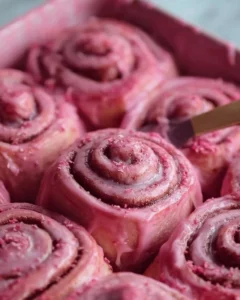 Pink Velvet Cinnamon Rolls topped with cream cheese frosting on a plate.