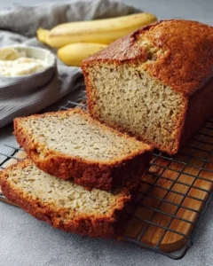 Slice of easy moist banana bread with ripe bananas on a wooden cutting board