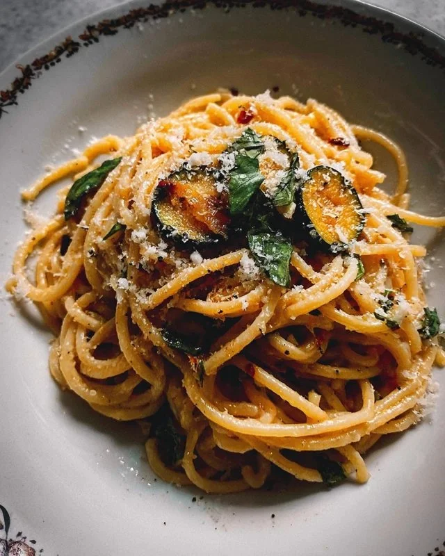 A plate of Nerano Spaghetti garnished with fresh basil and grated cheese.